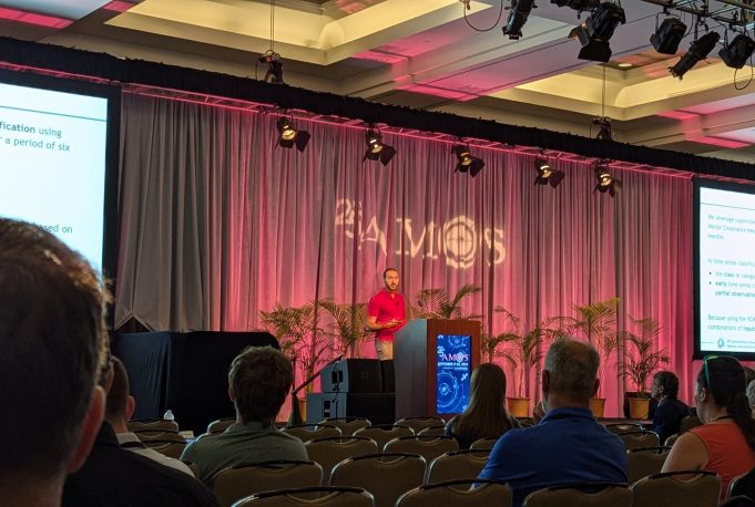 A member of ARCLab presenting on his project in front of a crowd with a screen on either side of him.