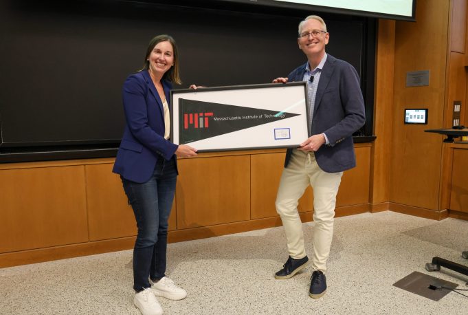 Two people holding a framed MIT pennant in front of a blackboard.